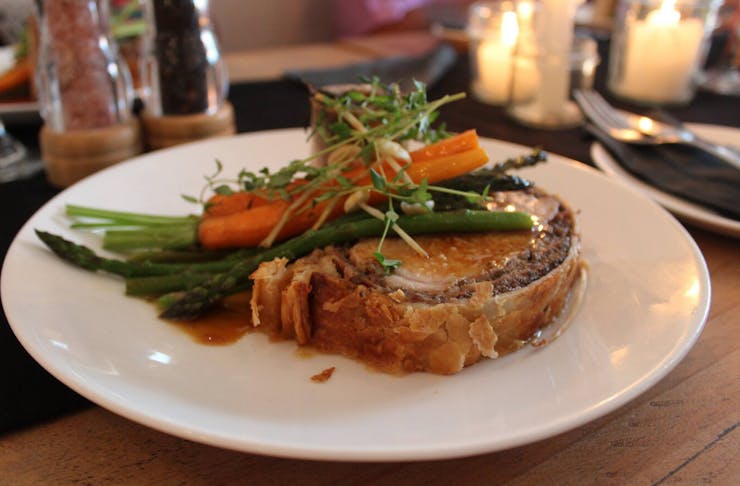Colourful main dish of pork wrapped in flaky bread crust topped with asparagus, carrots and microgreens