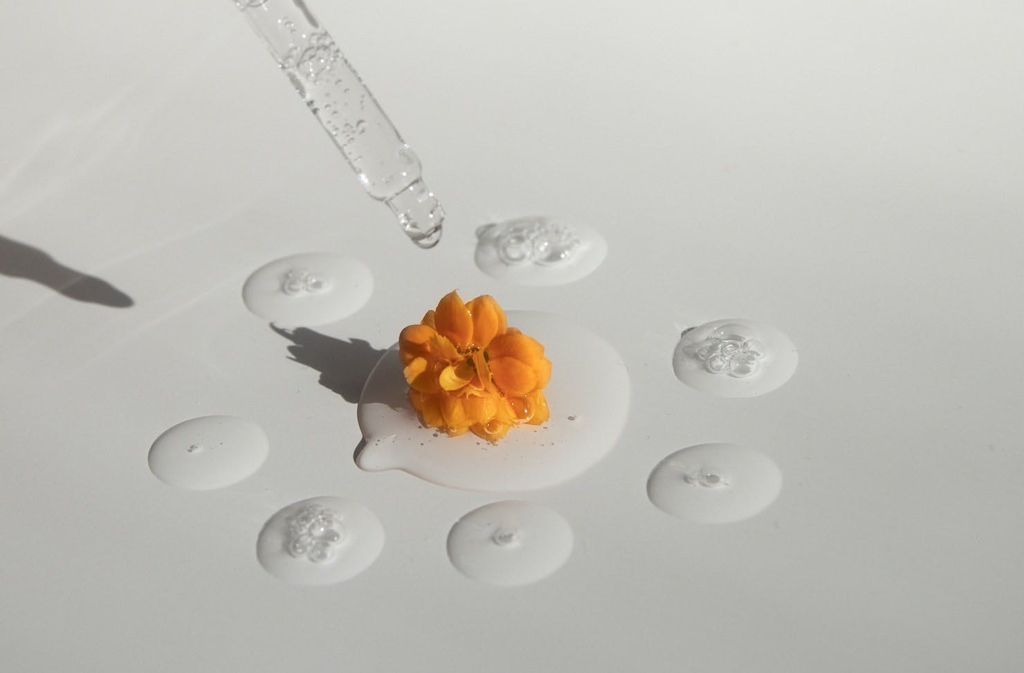 A series of drops of essential oil with an orange flower in the centre.
