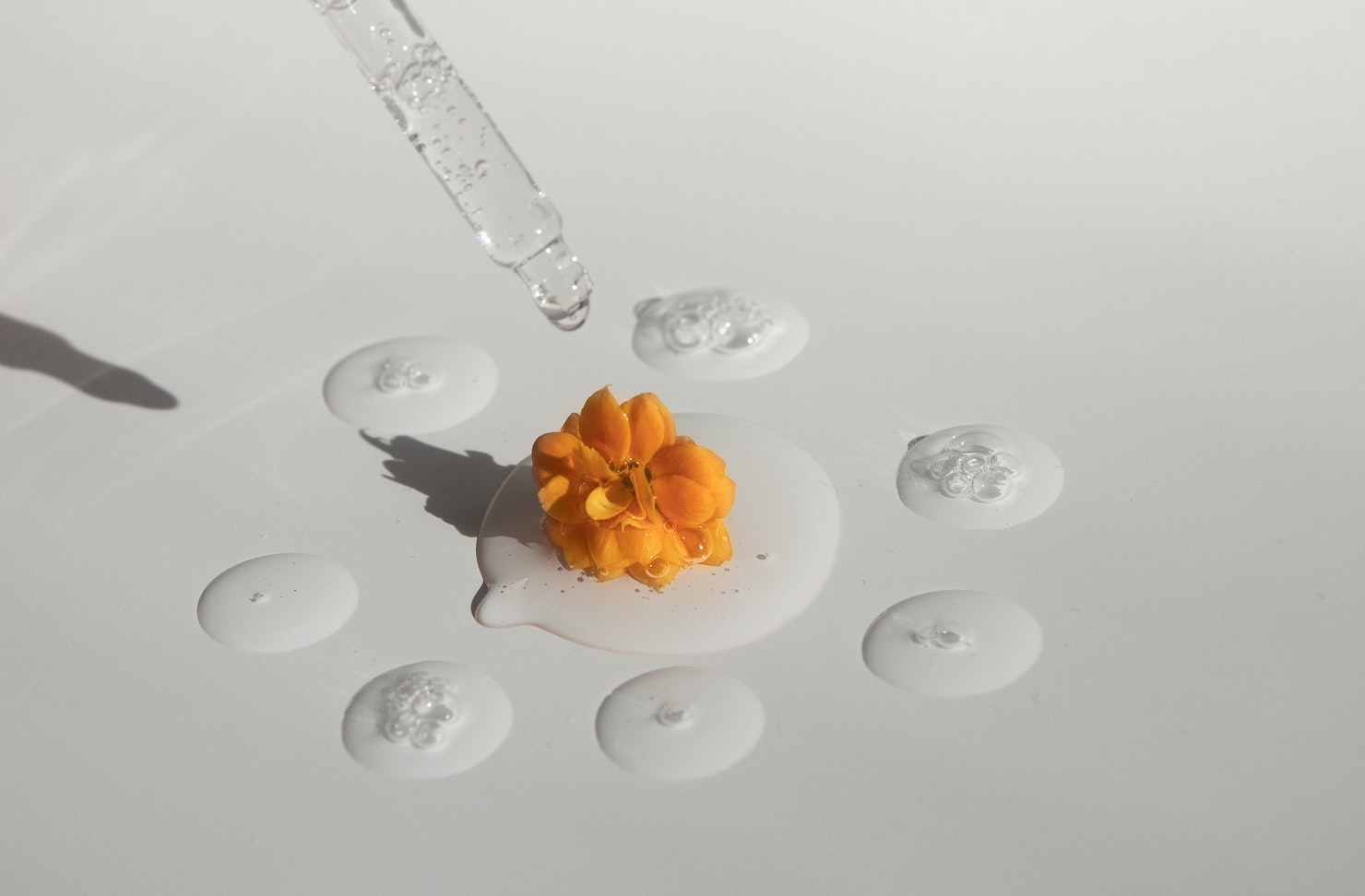 A series of drops of essential oil with an orange flower in the centre.