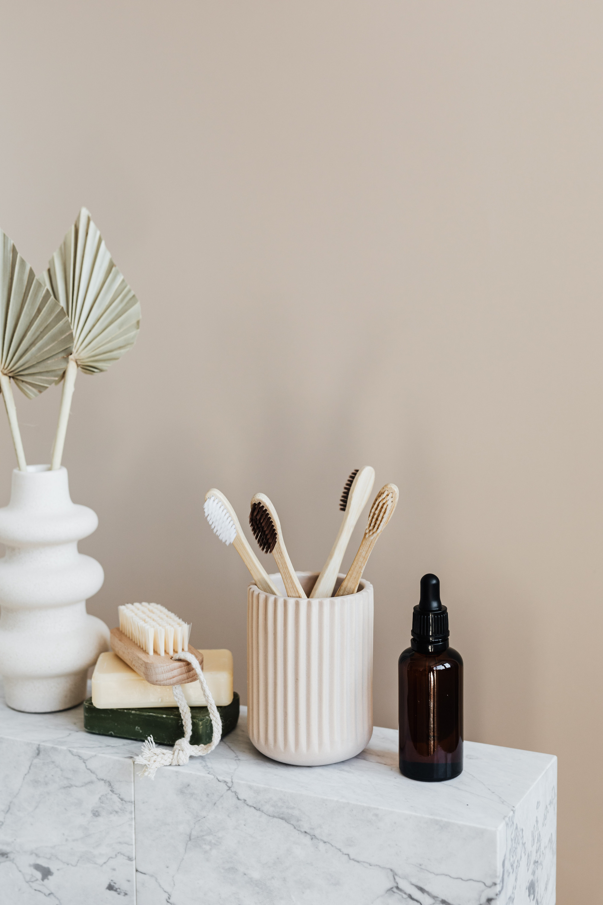A shot of four bamboo toothbrushes in a ceramic holder, alongside a serum bottle and a nail brush.