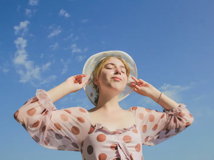 Woman standing in the sun with her eyes closed and a bucket hat on.