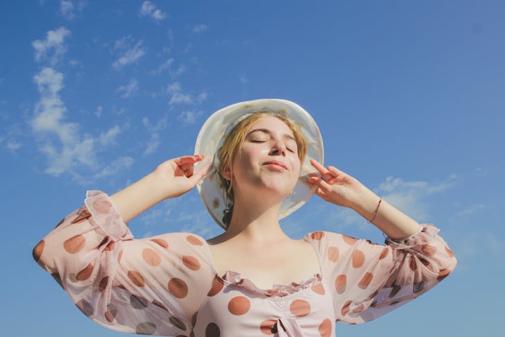 Woman standing in the sun with her eyes closed and a bucket hat on.