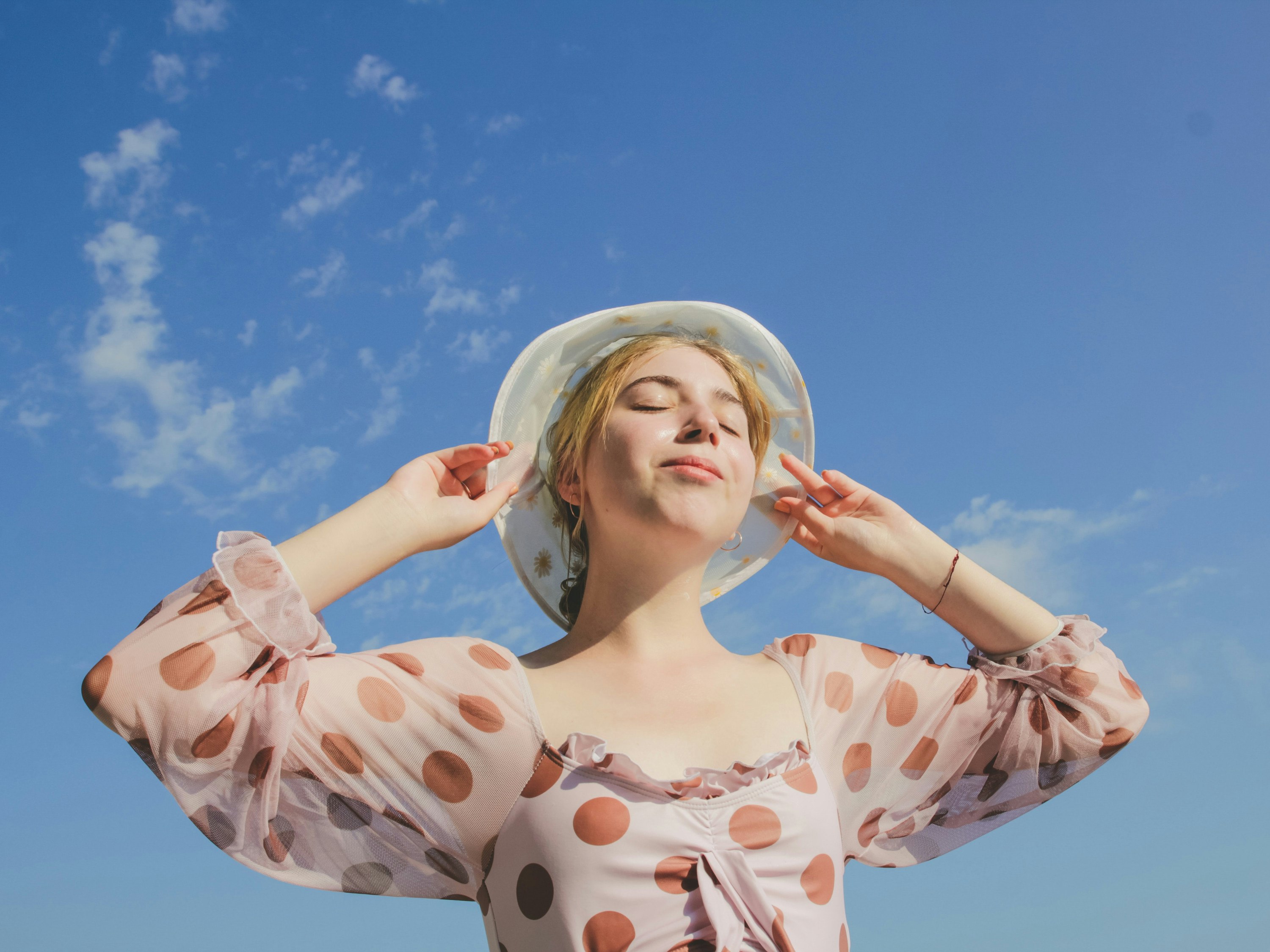 Woman standing in the sun with her eyes closed and a bucket hat on.