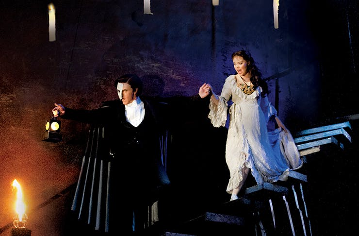 The Phantom of the Opera walking down a stone staircase holding a woman's hand.