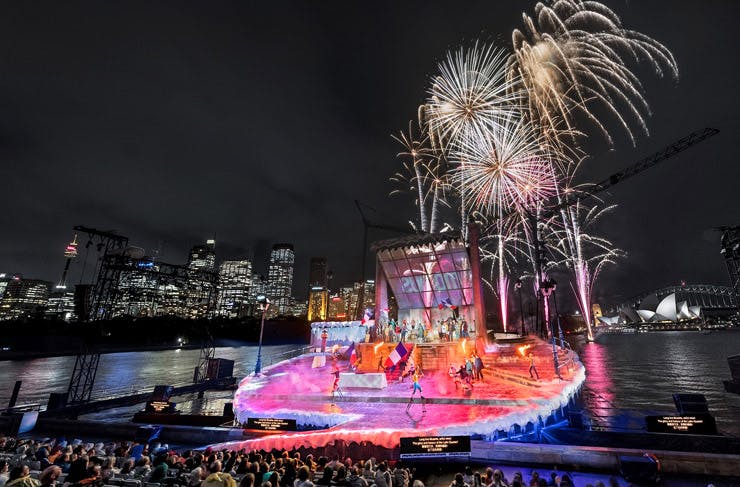 Fireworks over an outdoor stage, with Sydney Harbour in the background