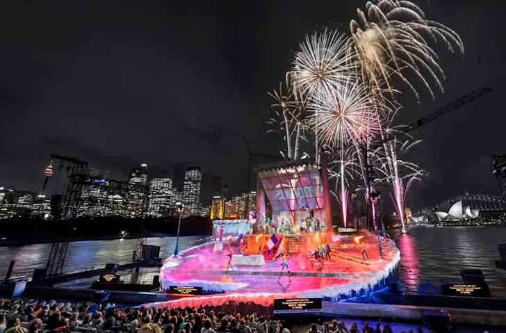 Fireworks over an outdoor stage, with Sydney Harbour in the background