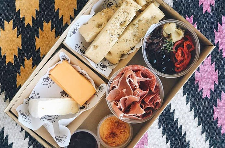 A cardboard box filled with cheese on a picnic rug