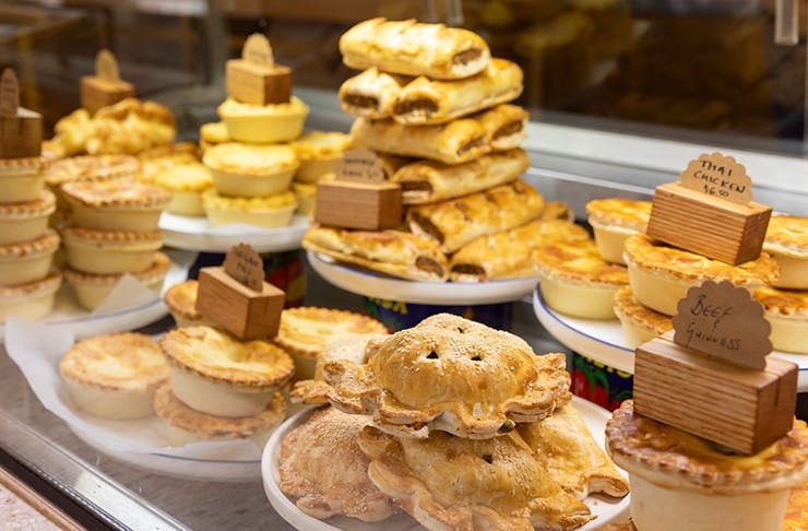 A glass display filled with various pies and sausage rolls.