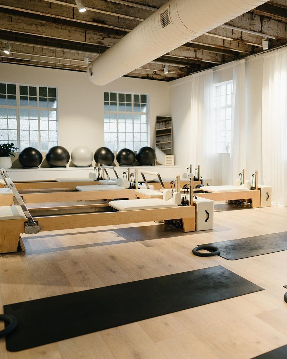 a brisbane pilates studio filled with white reformer beds under an industrial roof