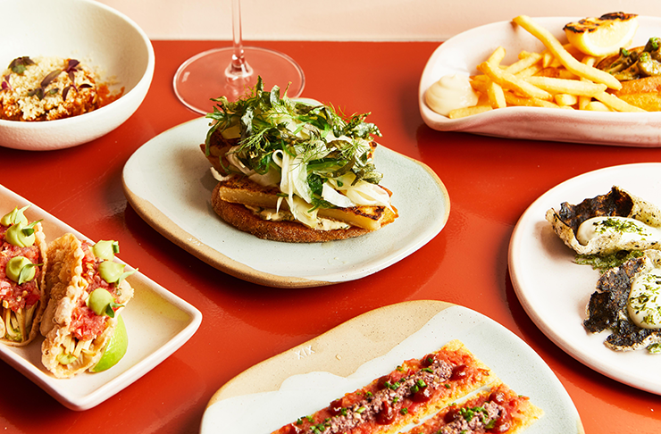 Several plates of seafood-inspired vegan dishes on an orange-y background.