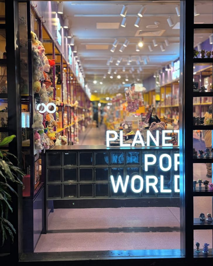 A picture from outside of the Planet Pop World store, with rows of floor to ceiling collectibles visible, and a giant neon sign reading 