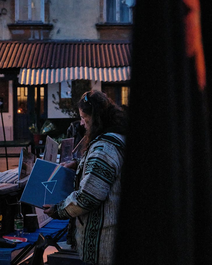 Someone with long hair in an eclectic jacket pulls out The Dark Side of the Moon from its iconic vinyl jacket at what seems to be an outdoor record market.