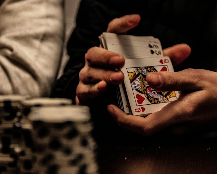 Someone shuffles a deck of cards, poker chips are stacked in the foreground.