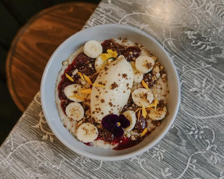 A round bowl on a table with muesli, yogurt, banana and edible flowers