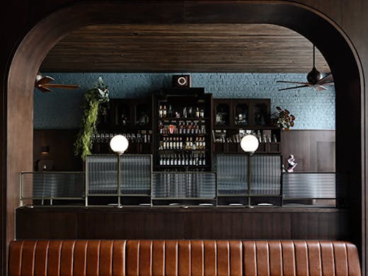 A long brown leather seat between two pillars. Poodle's bar can be seen in the background.
