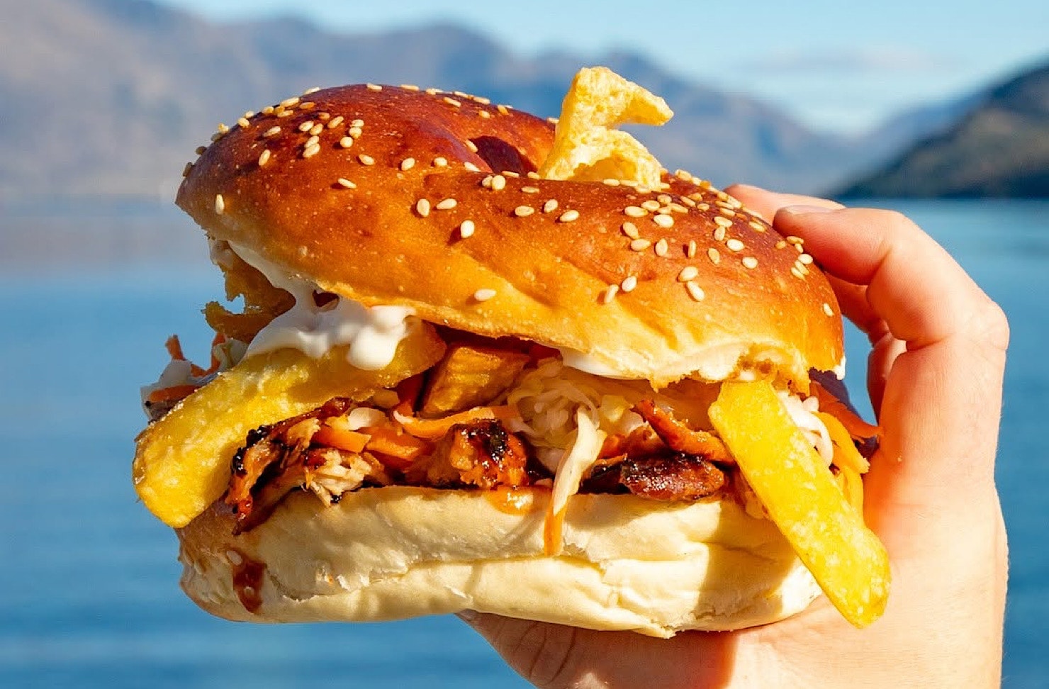 Someone holds a porkzilla 'burgel' against a beautiful lake backdrop. 