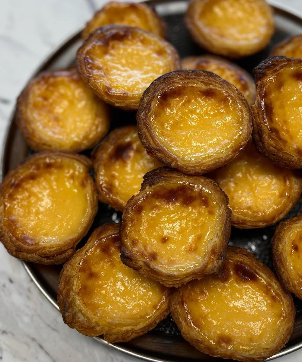 a silver plater stacked high with golden Portuguese tarts
