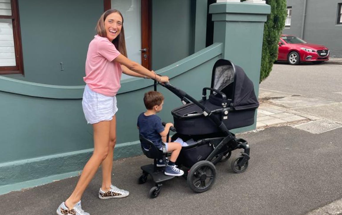 Lady smiling as she takes her kids for a walk in a pram along a street. 