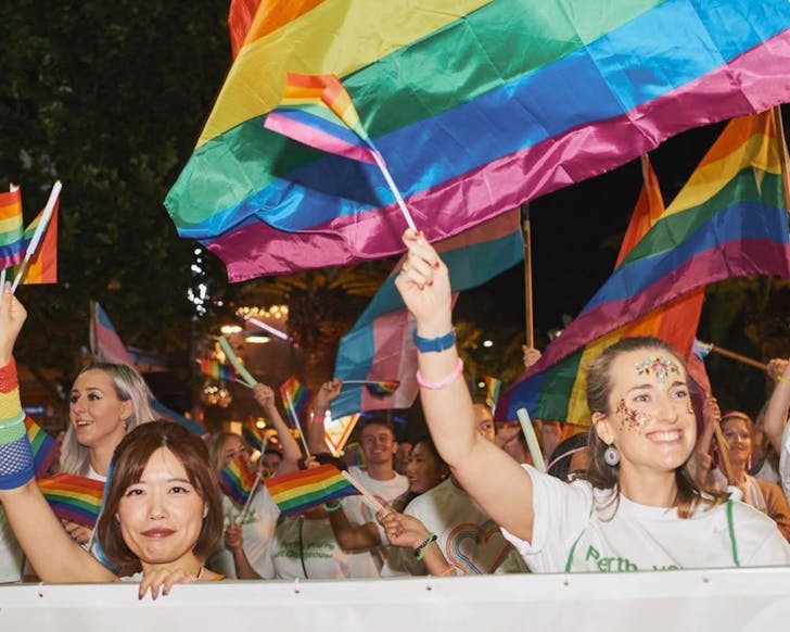 A group of women walk in the Perth Pride parade, waving rainbow flags