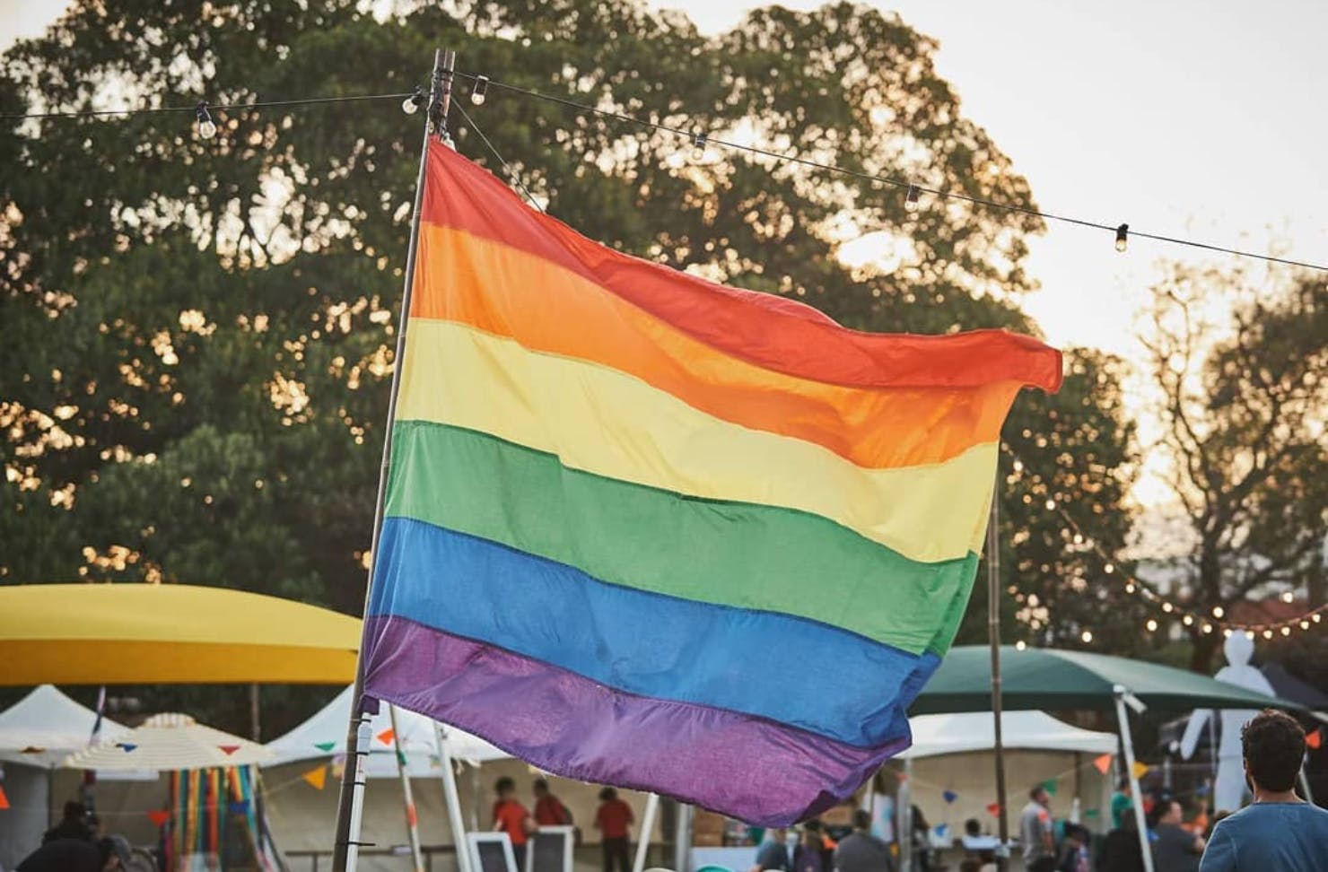 A rainbow pride flag waves against the sunset