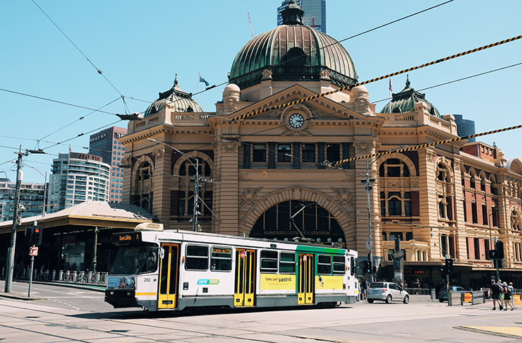 A tram passing by Flinders Street Station on a sunny day.