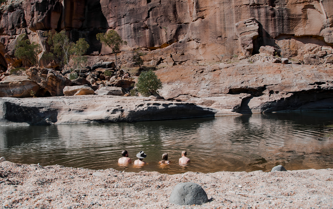 four people sitting in a watering hole under a cliff