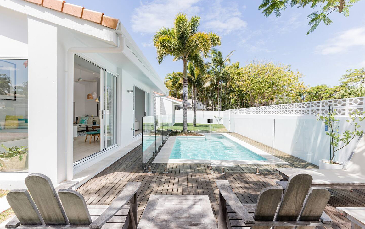 A white cottage with a pool in the side yard.