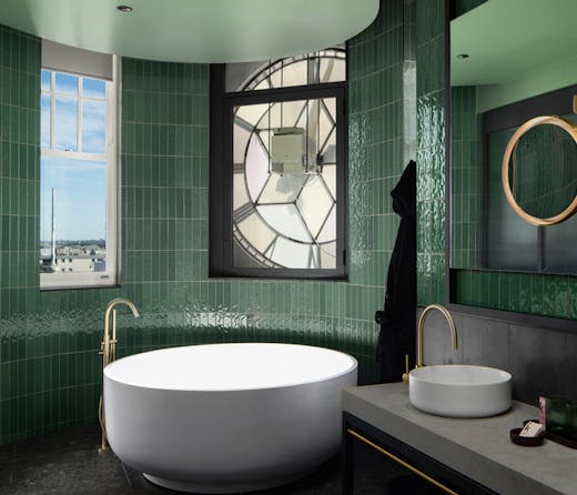 A large round bath tub in a bathroom with green tiles. 