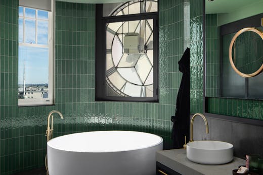 A large round bath tub in a bathroom with green tiles.