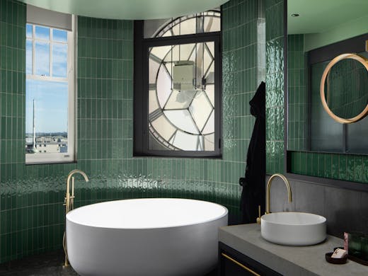 A large round bath tub in a bathroom with green tiles. 