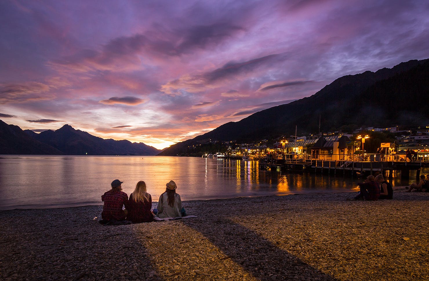 Three people watching the sunset on Queenstown Bay.