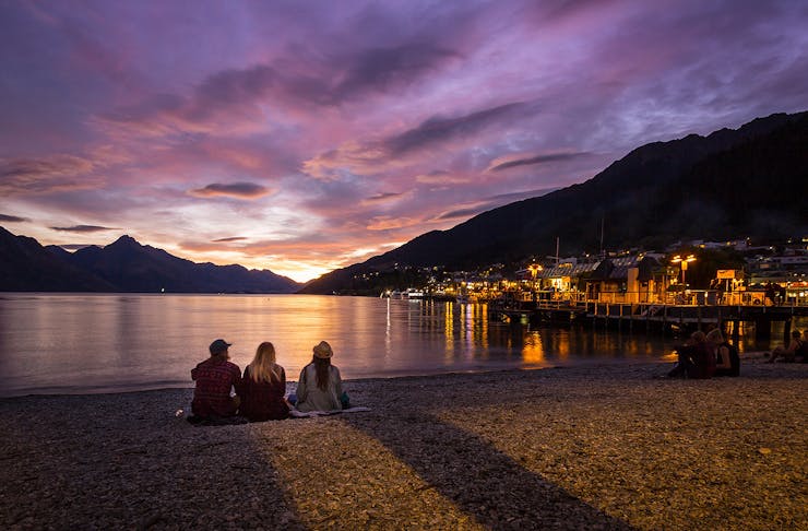 Three people watching the sunset on Queenstown Bay.