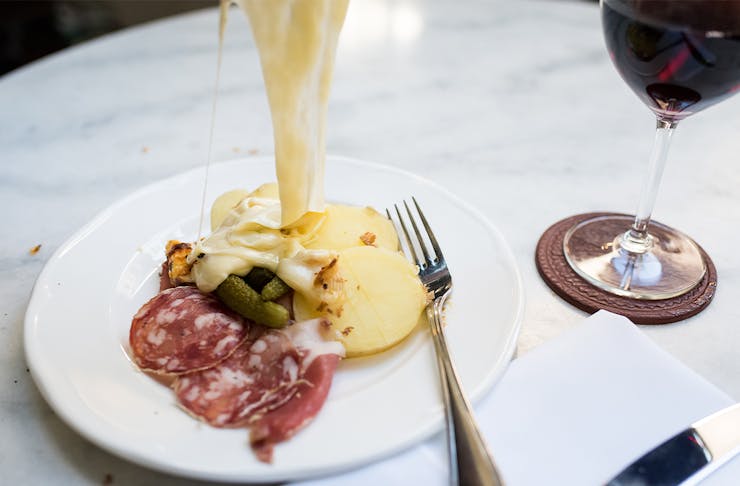 melted cheese being tipped on to a plate of potato, salami and pickles