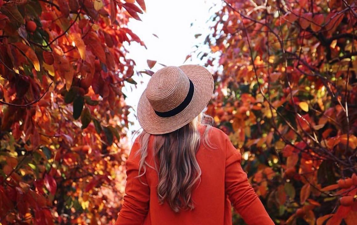 a woman dressed in a hat and red cardigan walks through Raeburn Orchards in the Perth Hills