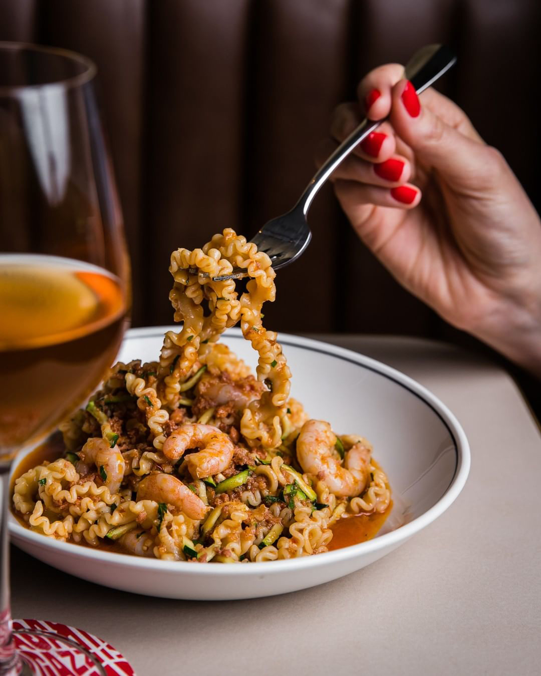 Fork with pasta noodle, bowl of pasta, and wine glass