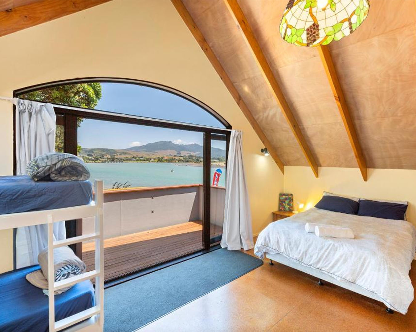 The interior of a well appointed room shows a window looking out to the sea with three beds.