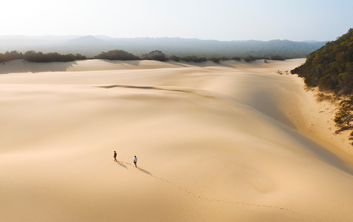 Two tiny people (far away) walking on a massive patch of sand, seen from above