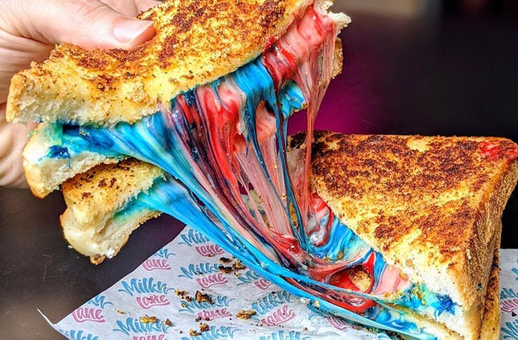 Two halves of a toastie filled with multi-coloured melted cheese being pulled apart.