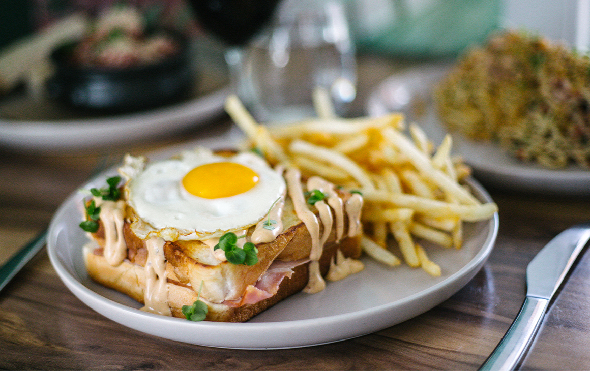 croque monsieur sandwich topped with egg and served on a plate with chips