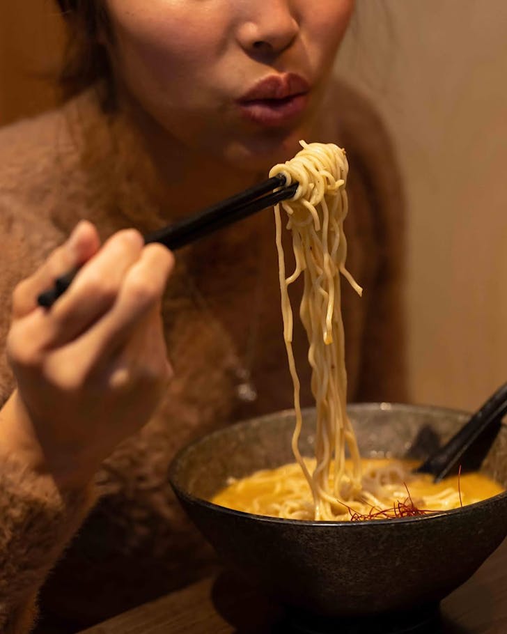 A woman blows on a long string of noodles.