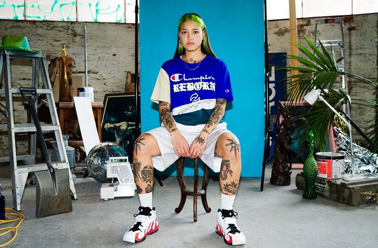 A girl sitting on a chair wearing the new REBORN x Champion up-cycled collection. 