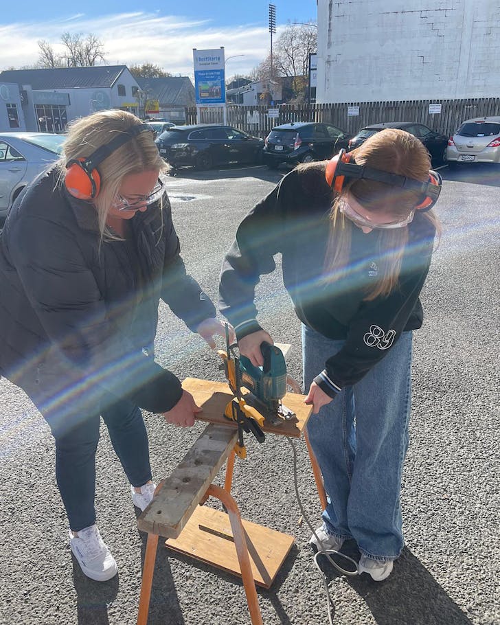 Two people saw some wood at a ReCreators workshop, in the morning sunshine.