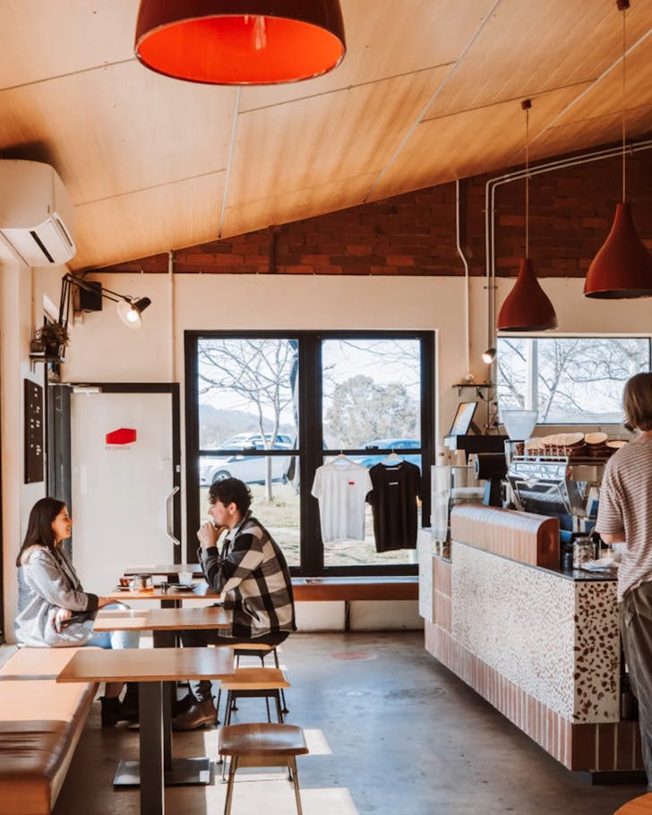 A wide shot of the interior of Red Brick cafe where a couple are seated talking over coffee and another person is standing by the coffee machine waiting for their drink. The place is well lit and welcoming.