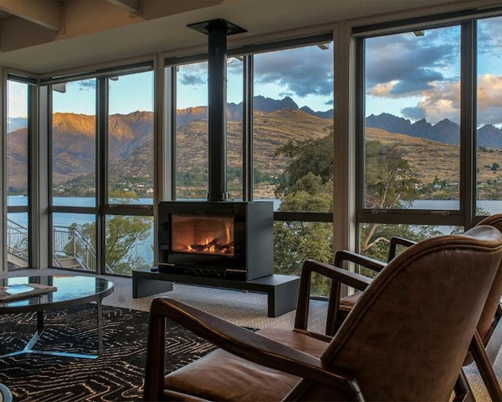 A view of an indoor fireplace burning in a room with a water view at The Rees Hotel & Luxury Apartments Queenstown