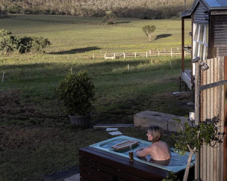 A woman lies in the outdoor bath at Boundary Rider Cabin Airbnb near Brisbane Queensland