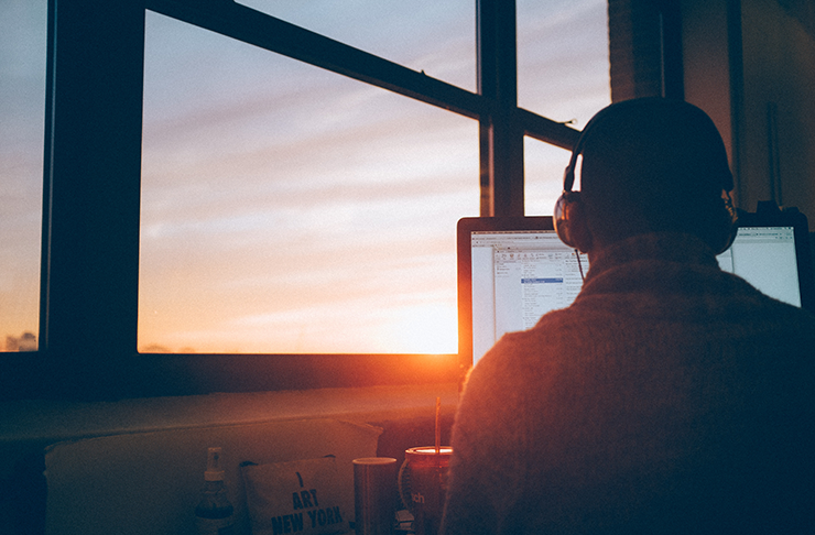 A person working on a computer by an office window. The afternoon sun is shining through.