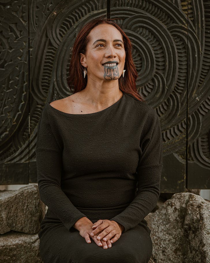 Ria Hall sits before a traditionally carved wall.