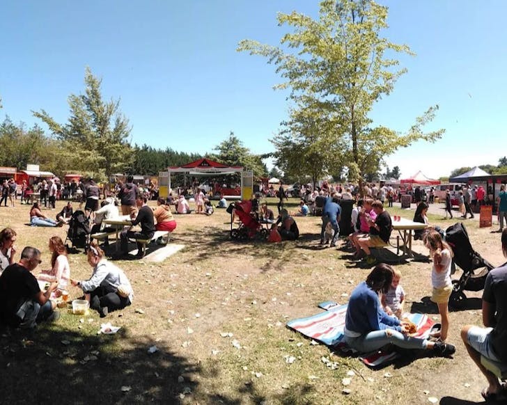 On a blue, sunny day, people sit around the massive grass area of The Riccarton Market.