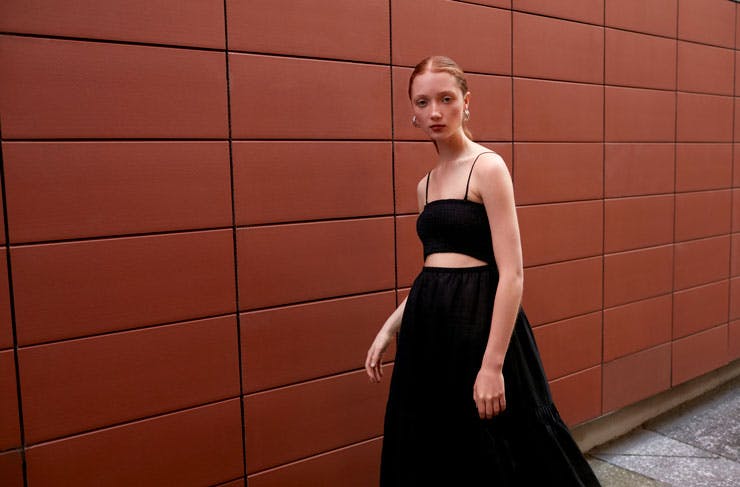 A model in a long black dress against a tiled wall