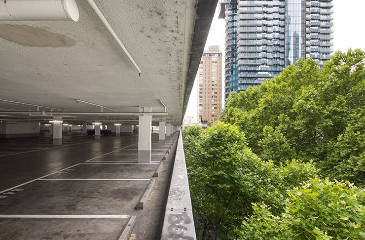 A rooftop carpark in Melbourne CBD. Several trees and the citt skyline can be seen in the background.